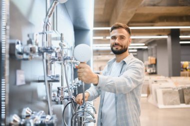 Delikanlı, yeni duş başlığı ve tesisat ekipmanlarını bir mağazada seçiyor ve kameraya gülümsüyor.