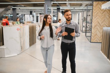 Kadın ve erkek, büyük bir fayans ve döşeme mağazasında yenileme seçeneklerini tartışıyor, ev geliştirme üzerine odaklanıyorlar.