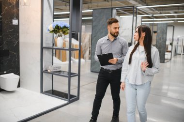 Genç bir bayan müşteriye fayans örnekleri gösteren erkek danışman ev yenileme seçeneklerini tartışıyor.