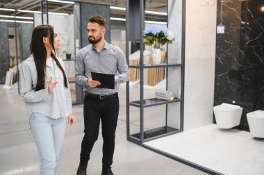 Müşteri, bir hırdavatçıda bir satış danışmanıyla yenileme fikirlerini tartışıyor, banyo kiremitleri ve eşyalar seçiyor.