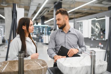 Kadın ve satıcı ev tadilatı için yeni lavaboları tartışıyorlar. Modern bir perakende satış mağazasında banyo malzemeleri seçiyorum.