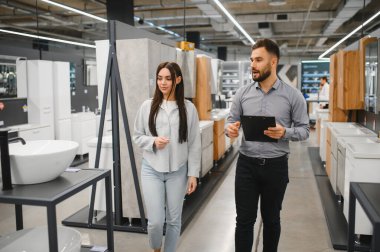 Hırdavatçı, yeni bir banyo tadilatı için genç bir bayana yardım ediyor ve ev geliştirme seçeneklerini tartışıyor.
