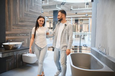 Bir galeride yeni banyo malzemeleri arayan genç bir çift gülümsüyor ve evi yenilemek için hoş bir alışveriş deneyimi yaşıyor.