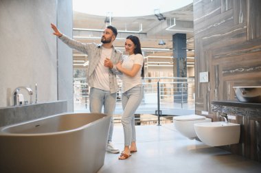 Genç çift küvet ve fayans seçiyor, büyük bir ev geliştirme galerisinde banyo tadilatı yapmayı planlıyor.