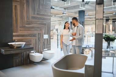 Genç çift yeni banyo tadilatını tartışıyor, bir ev geliştirme mağazasındaki modern hijyenik yazılımlara ve fayanslara bakıyor