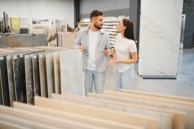 Bir hırdavatçıda yeni fayanslar seçen genç çift, ev geliştirme ve döşeme seçeneklerini tartışıyor