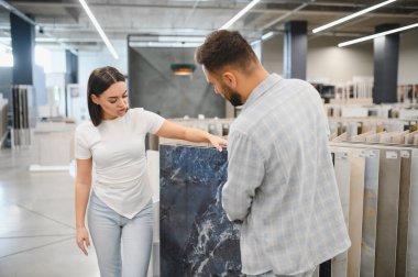 Genç bir çift bir hırdavatçıda seramik döşeme seçiyor, ev geliştirme ve yenileme seçeneklerini tartışıyorlar.