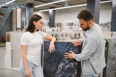 Ev geliştirme projesi için büyük format mavi mermer efekt fayanslarını inceleyen çift. İç mekan için önemli tasarım kararları almak