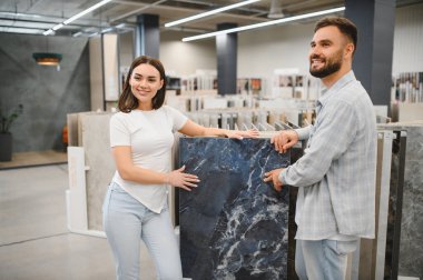 Genç çift, yeni bir ev geliştirme projesi için mermer ve taş döşeme seçiyor ve yenileme çalışmaları için gülümsüyor.