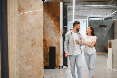 Genç bir çift bir galeride yürüyor, ev dekorasyonu projesi için yeni fayanslar tartışıyor ve seçiyorlar.