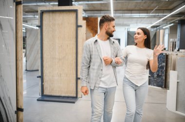 Mutlu çift kol kola, fayans galerisinde yürüyorlar, yeni evleri için çeşitli zemin ve duvar seçeneklerini araştırıyorlar.