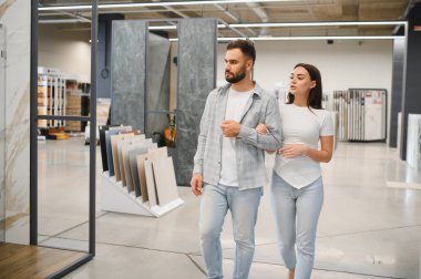 Parlak bir sergi salonundaki döşeme ve duvar fayanslarını karşılaştıran genç bir çift, apartman yenilemeyi ve şık malzemeler seçmeyi planlıyorlar.