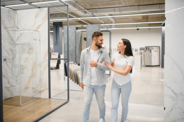 Genç çiftler çağdaş sergi salonlarına bakıyorlar, örnekleri karşılaştırıyorlar ve yeni evleri için modern bir banyo yenilemesi planlıyorlar.