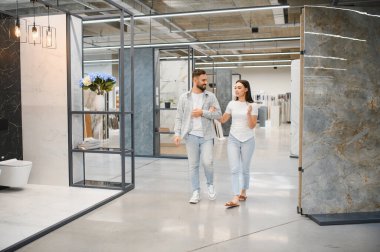 Ev geliştirme sergisinde yürüyen ve konuşan çift, yeni ev projeleri için farklı döşeme ve duvar döşemelerine bakıyorlar.