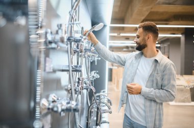 Banyo malzemeleri için alışveriş yapan bir adam, bir ev geliştirme mağazasından çok çeşitli seçenekler arasından duş başlığı seçen bir adam.