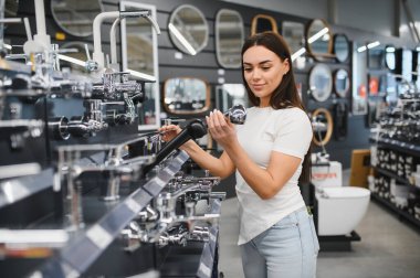Banyo tamiri için duş başlığı ya da musluğu seçen bir kadın. Ev geliştirme projesi ve tesisat malzemeleri için perakende alışveriş