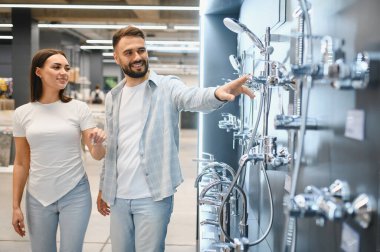 Mutlu çift yeni banyo eşyaları için alışveriş yapıyor. Modern bir hırdavatçıda sergilenen duşa bakan adam.