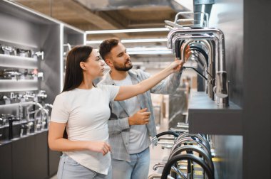 Genç bir çift banyo veya mutfak yenilemesi için yeni musluklar seçiyor, modern bir perakende galerisinde sergilenen ürünleri inceliyor