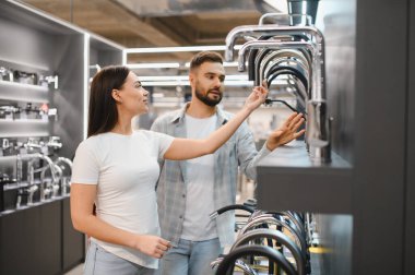 Genç çift hırdavatçıdan yeni mutfak veya banyo muslukları seçiyor. Ev geliştirme projesi için malzeme seçiliyor