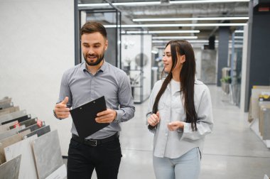 Satıcı, müşteriye inşaat malzemeleri mağazasında yeni döşeme seçmesinde yardım ediyor. Ev geliştirme ve yenileme kavramı