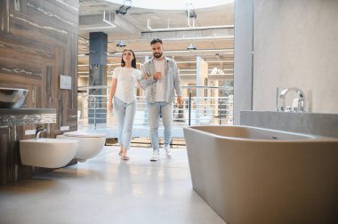 Bir çift banyo galerisinde yürüyor, küvetlere, tuvaletlere ve evlerini yenilemek için lavabolara bakıyor.