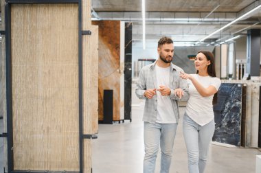 Genç çift tartışıyor ve işaret ediyor, seramik mağazasında ev geliştirme projesi için yeni fayanslar seçiyorlar.