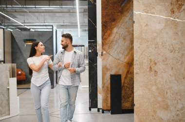 Kol kola yürüyen genç bir çift, çeşitli mermer ve granit levhalara bakıyor, bir taş dükkanında yenileme kararları alıyorlar.