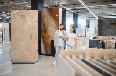 Genç bir çift sergi salonunda yürüyor, yeni döşeme ve malzemeler arıyorlar ev geliştirme projeleri için