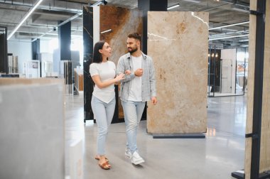 Genç bir adam ve kadın bir sergi salonunda yürüyor, ev geliştirme ve tasarım projesi için büyük örneklere bakıyor.