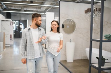 Genç bir çift modern bir banyo galerisinde yürüyor, evleri için geliştirme seçeneklerini tartışıyorlar.