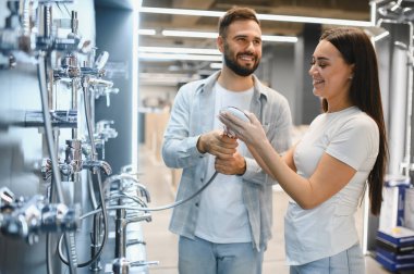 Duş başlıkları ve musluklara bakan genç bir çift, bir ev geliştirme mağazasında banyo yenileme malzemeleri seçiyorlar.