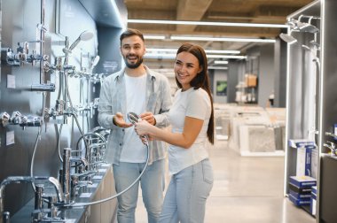 Mutlu çift hırdavatçıdan yeni bir duş başlığı seçiyor, gülümsüyor ve banyo yenileme planları yapıyor.