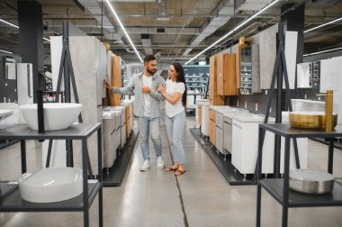 Modern banyo süslemelerini ve lavabolarını karşılaştıran genç bir çift, bir ev yenileme projesi planlarken ve tesisat seçerken...