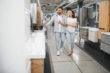 Modern banyo süslemelerini ve lavabolarını gezen bir çift, bir sergi salonunda ev yenileme ve projeleri için eşyalar tasarlıyorlar.