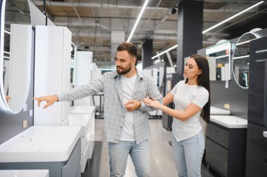 Ev dekorasyonu için yeni banyo mobilyaları alırken, genç çift lavabo ve aynayı seçiyor.