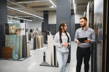 Müşteri, bir hırdavatçı reyonunda bir danışman ile iletişim kuruyor ve ev geliştirme için yeni fayanslar seçiyor.