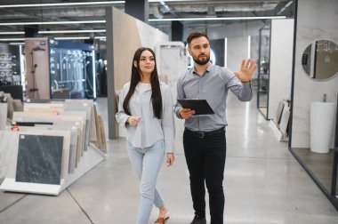 Perakende işçisi, modern bir mağazada yeni kat ve duvar örtüleri seçen bir kadına yardım ediyor.