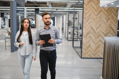 Kadın ve erkek modern bir galeride yürüyor, ev yenileme ve iç tasarım projeleri seçeneklerini tartışıyorlar.