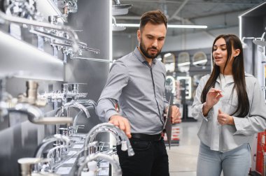 Genç bir bayana tavsiye veren erkek satış elemanı, evinin tadilatı için farklı mutfak ve banyo tesisatlarını karşılaştırıyor.