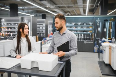 Satış asistanı, bir hırdavatçıda yeni banyo seçen bir bayana ev geliştirme konusunda yardım ediyor.