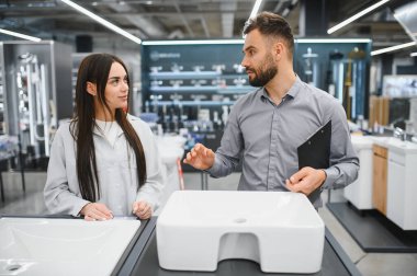 Satış asistanı bayan müşteriye ev banyosu yenileme projesi için bir hırdavatçıda yeni bir lavabo seçmesinde yardım ediyor.