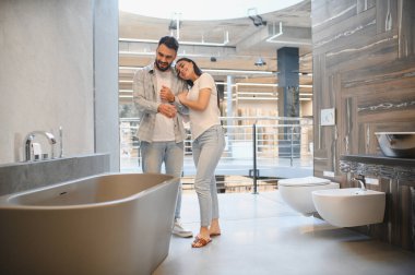 Genç bir çift banyo galerisinde modern bir küvete bakıyor. Birlikte tadilat yapmayı planlıyorlar.