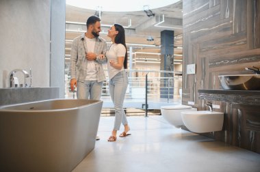 Bir çift banyo galerisinde yürüyor, ev tadilatı ya da yeni ev projesi için eşyalar ve fayanslar seçiyor.