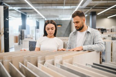 Evde tadilat için farklı fayans örneklerini karşılaştıran genç bir çift. Perakende satış mağazasında yer almak için alışveriş yapıyorlar.