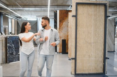 İnşaat malzemeleri için alışveriş yapan genç bir çift, büyük bir galeride doğal taş fayanslar ve levhalar seçiyorlar.