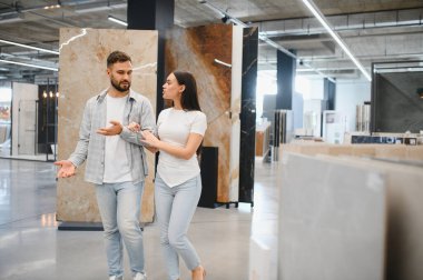 Genç bir çift, yeni evleri için ev dekorasyonu mağazasında yer ve duvar döşemesi alışverişi yapıyor.