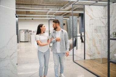 Genç bir çift, banyo ya da mutfak yenileme için seramik fayanslar seçerek, bir mağazanın vitrininde yürüyor.