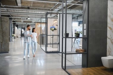 Modern bir galeride yürüyen genç bir çift yeni evleri için farklı fayanslar ve banyo armatürlerini keşfediyor.