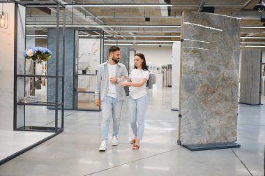 Birlikte yürüyen genç bir çift, bir ev yenileme projesi için geniş format porselen ve seramik döşeme fayanslarına bakıyor