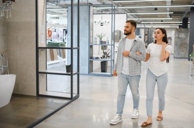 Genç bir çift modern bir ev geliştirme mağazasında banyo eşyaları ve fayanslar arıyor, bir ev yenileme planı yapıyorlar.